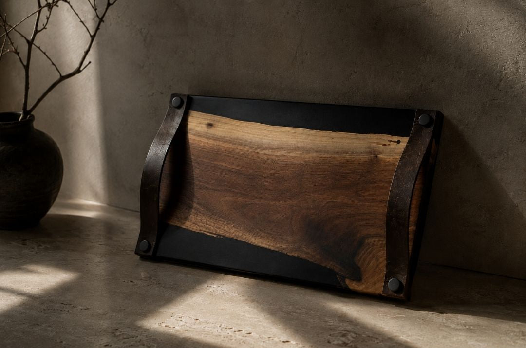 Wooden serving board with leather adn metal accents on a concrete floor with a vase in the background